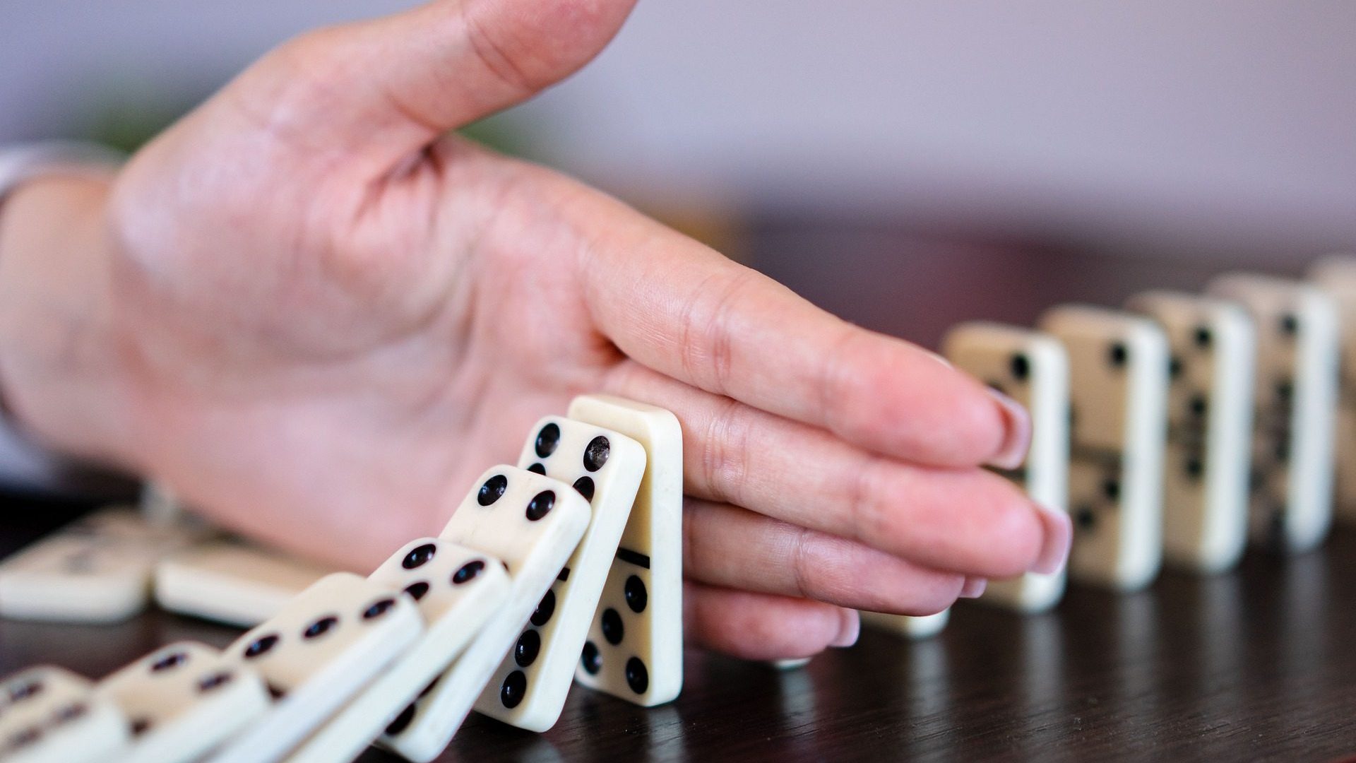 A hand stopping falling dominoes before the problem spreads
